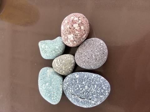Six polished, multicoloured pebble stones displayed on a brown tabletop.