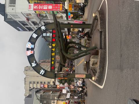 An arched green steel bus shelter with colourful LED text stands on a small-town street.