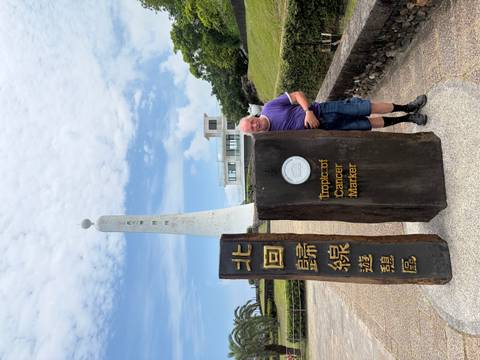 Man beside stone pillars marking the Tropic of Cancer monument under a partly cloudy sky.