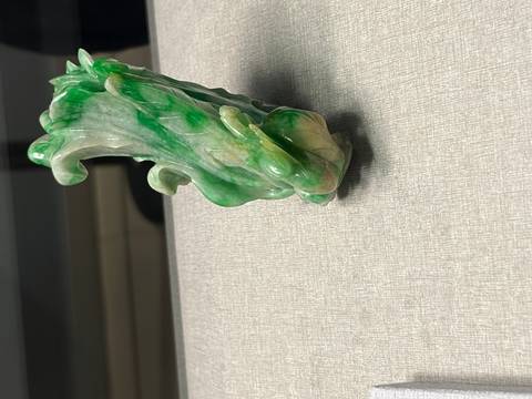 A small jadeite carving resembling a cabbage displayed on a neutral fabric surface.