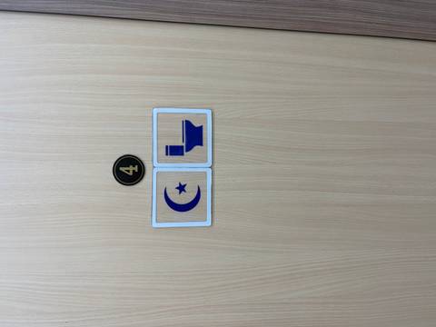 Minimalist door sign combining a crescent-star symbol and toilet icon under the number 4.