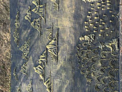 Bronze relief panel depicting rice fields, farmers, and mountains in shallow perspective.