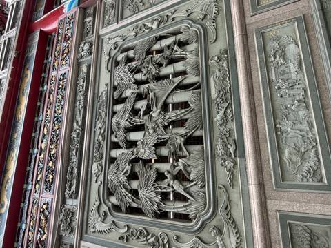 Detailed stone carving on a temple façade depicting birds among bamboo and figures below.