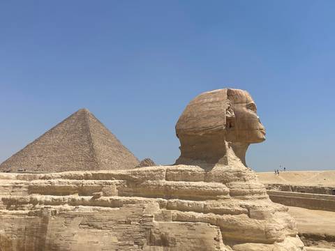 Iconic profile view of the Great Sphinx with the Pyramid of Khafre and desert sands under a clear blue sky.