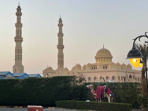 Evening view of an ornate waterfront mosque with twin minarets and a lit street lamp in the foreground.