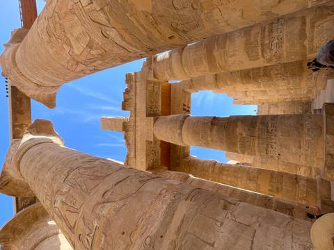 Up-angle shot between colossal hieroglyph-covered columns in Karnak Temple with blue sky peeking through.