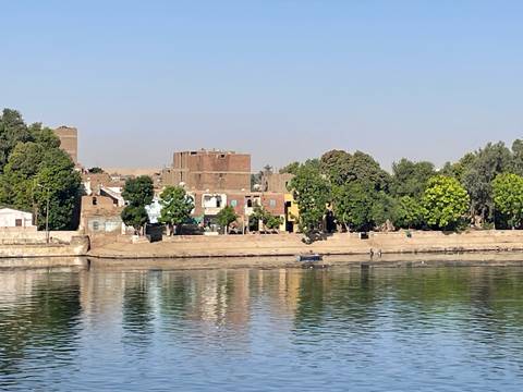 Calm morning view of traditional brick homes and lush trees lining the Nile River bank.