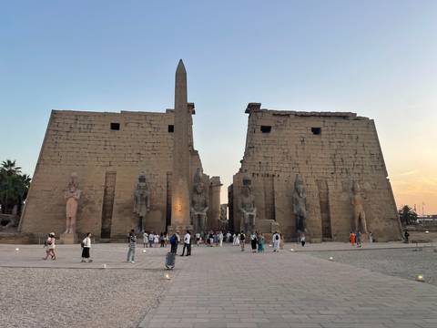 Luxor Temple entrance with obelisk at dusk, softly lit with tourists gathering in the courtyard.