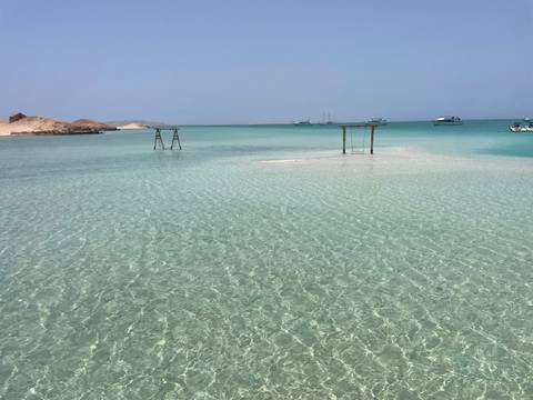 Crystal-clear turquoise shallows with small jetties and tour boats floating near a sandy islet.