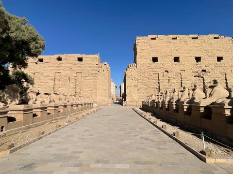 Symmetrical avenue of ram-headed sphinxes leading to the first pylon of Karnak Temple beneath a clear blue sky.