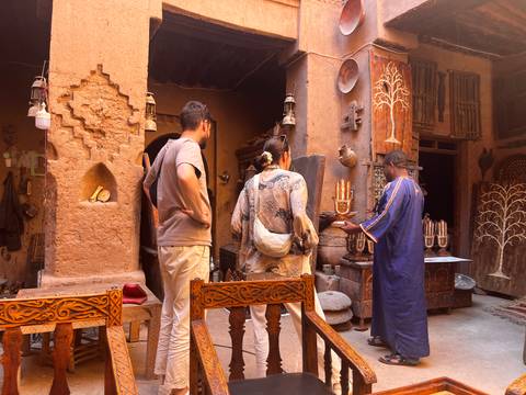 Travelers interact with a local artisan inside an atmospheric earthen Kasbah filled with traditional Berber crafts.