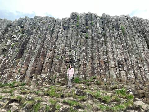 Traveler stands at the foot of towering basalt columns of the Giant's Causeway formation.