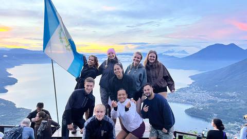 Happy group posing with national flag atop viewpoint overlooking Lake Atitlán at sunrise