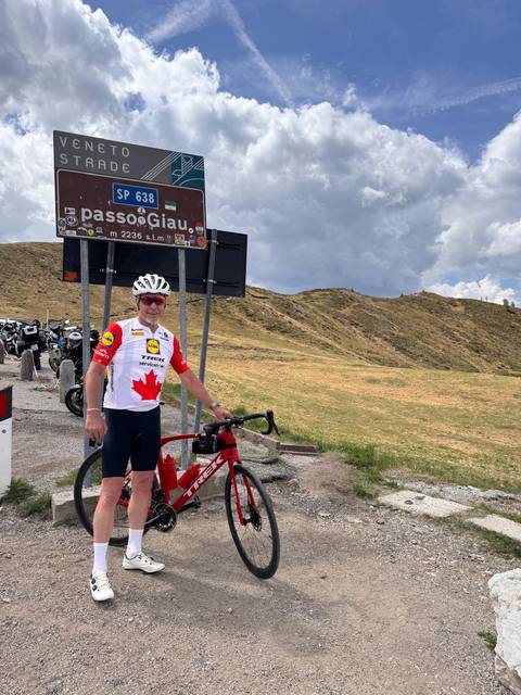 Cyclist posing with bike at Passo Giau summit sign in the Dolomites