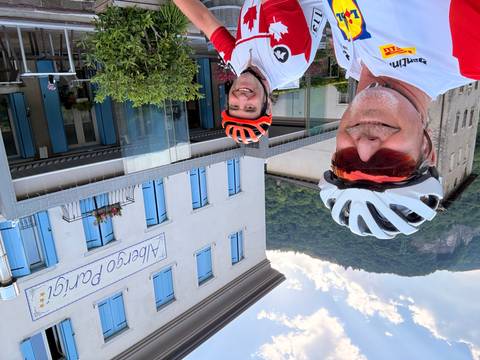 Two cyclists smiling outside Albergo Parigi hotel with forested hillside backdrop