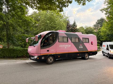 Iconic pink Giro d'Italia team bus driving along tree-lined road