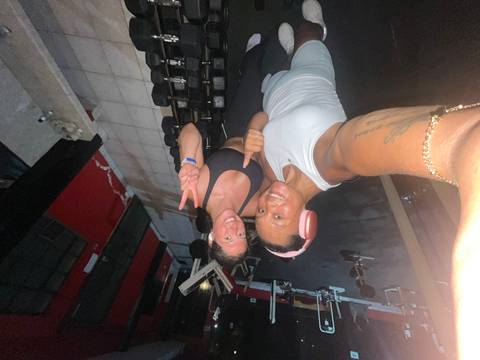 Two women taking selfie inside basic gym with free weights visible