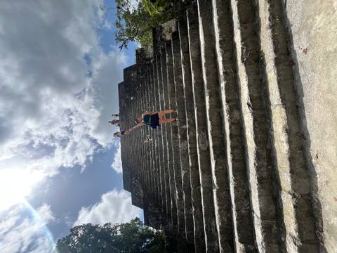 Woman halfway up massive stone pyramid steps with others at the top under bright sun