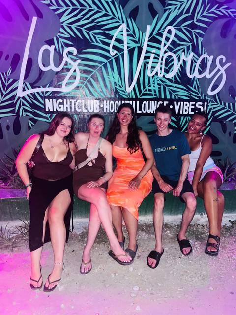 Friends sitting on a bench at night in front of a nightclub lounge vibes sign