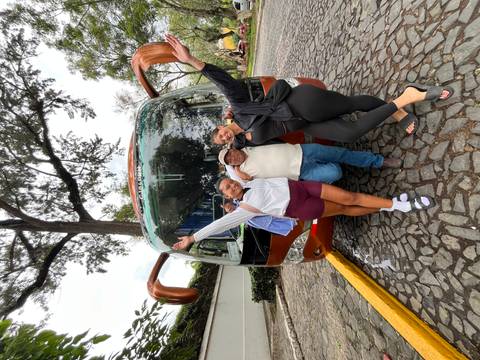 Two women and a friendly driver posing in front of a tour coach on cobblestone street