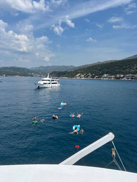 Small cruise boat anchored while swimmers float and relax in clear Adriatic waters