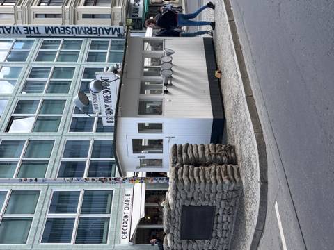 Historic Checkpoint Charlie guardhouse with sandbags and sign on a Berlin street corner.