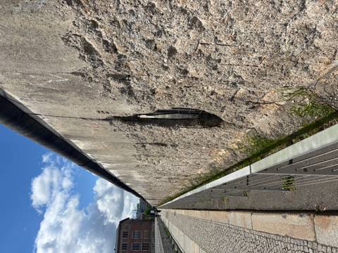 Close perspective of a weather-worn section of the Berlin Wall with a large hole and blue sky above.