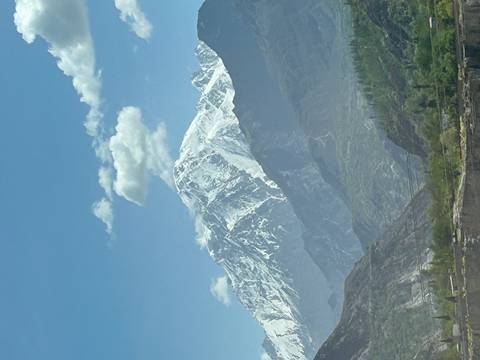Snow-capped mountain peak rising above layered green and rocky valleys under a clear blue sky.