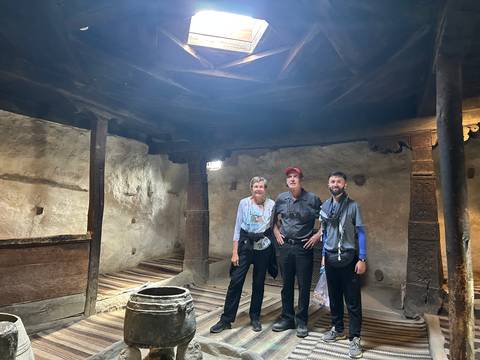 Three travellers pose inside a centuries-old wooden-roofed hall with carved pillars.