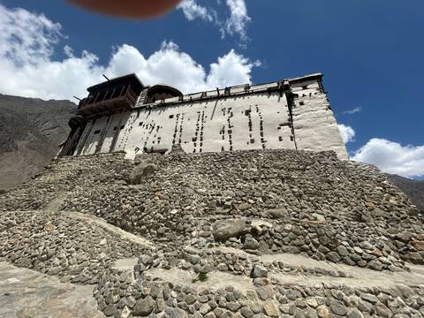 Stone ramparts leading up to the white-walled Baltit Fort against a blue sky.