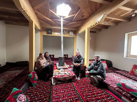 Group enjoys tea and snacks while seated on colourful carpets inside a traditional home.