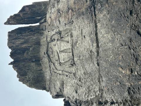 Ancient Buddha figure carved into a tall, dark rock cliff.