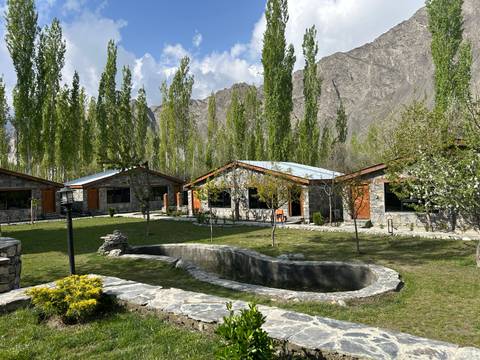 Stone cottages and manicured lawns with a small pond set against tall poplar trees and mountains.