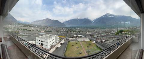Wide panoramic cityscape framed by balcony railings with mountains rising behind the valley town.