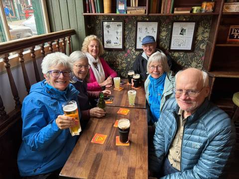 Group of travellers in a cozy Irish pub raising glasses of beer and cider at a wooden table.