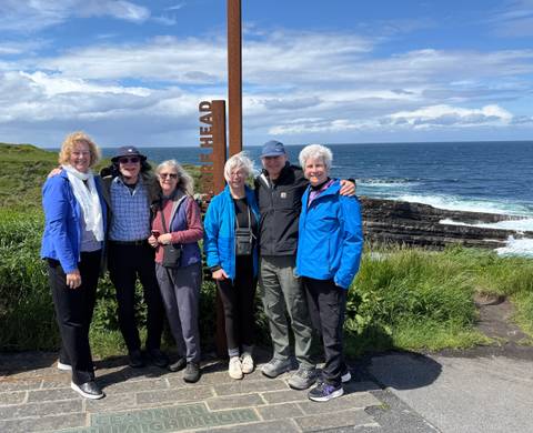 Travellers posing by a rusty Sliabh Liag viewpoint sign with dramatic Atlantic cliffs behind.