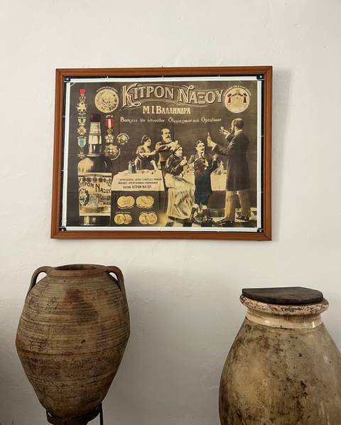 Vintage advertisement poster displayed above rustic pottery jars in a small museum corner.