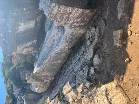 Massive unfinished ancient marble statue lying in a rocky quarry, weathered and cracked.