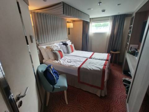 Compact river-cruise cabin with twin beds neatly made, soft lighting and a small window.