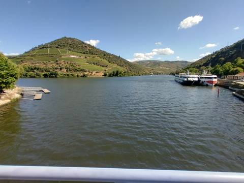 Wide Douro River flanked by terraced hillsides with two river-cruise boats docked under a bright sky.