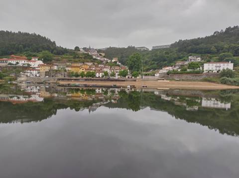 Quaint riverside village reflected perfectly on glassy water beneath a brooding grey sky.
