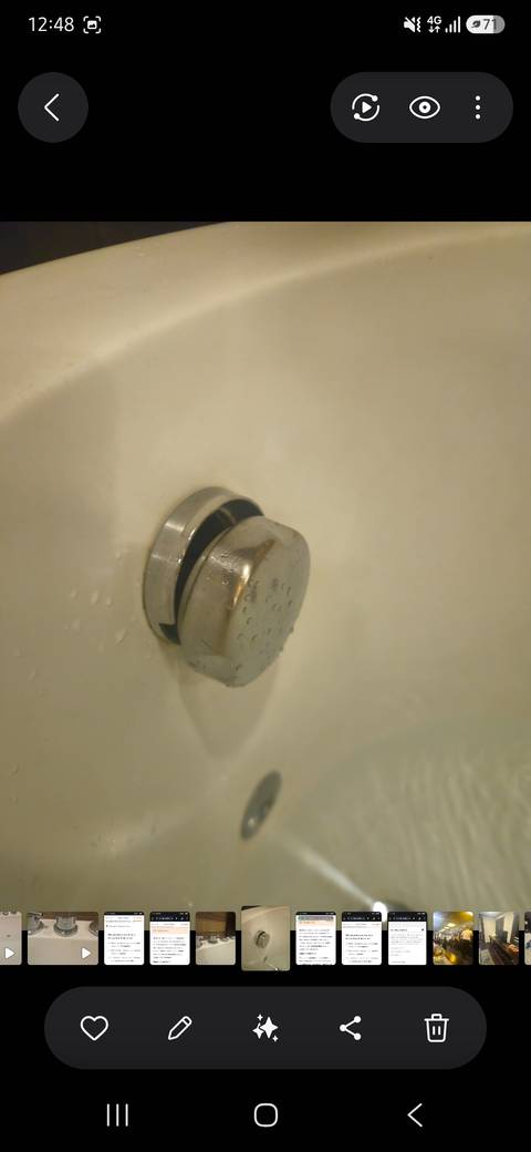 Blurry close-up of a metal bathtub plug against a pale background with water droplets.