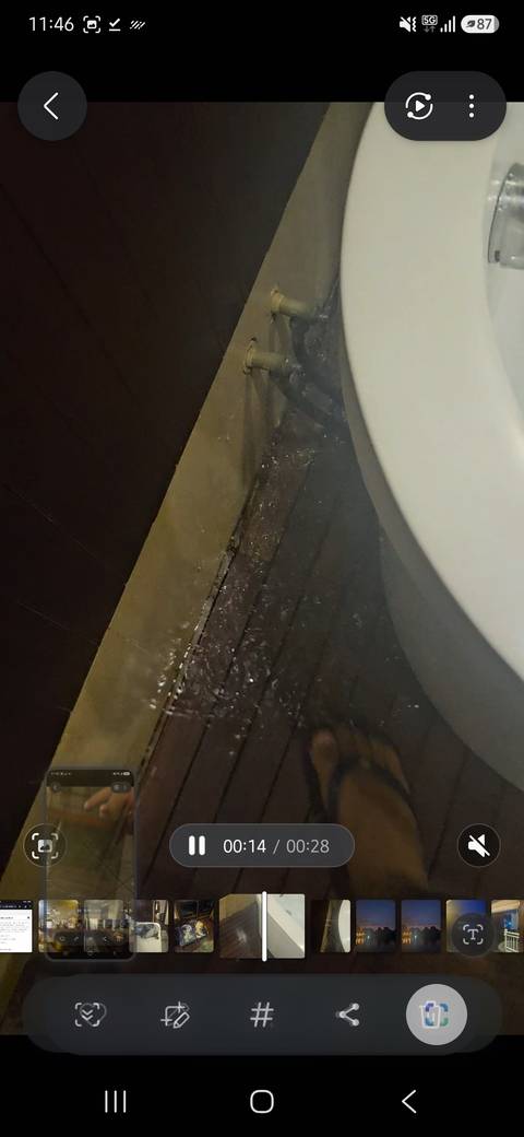 Low-quality photo of water pooling on a dark bathroom floor near a toilet bowl.