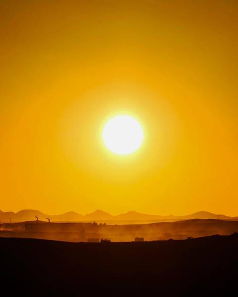 Large blazing sun dominates a hazy orange desert sky above distant hills.
