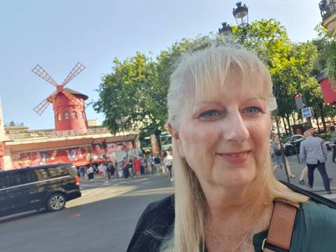 Close-up selfie of a woman in front of the red windmill at the Moulin Rouge in Paris.
