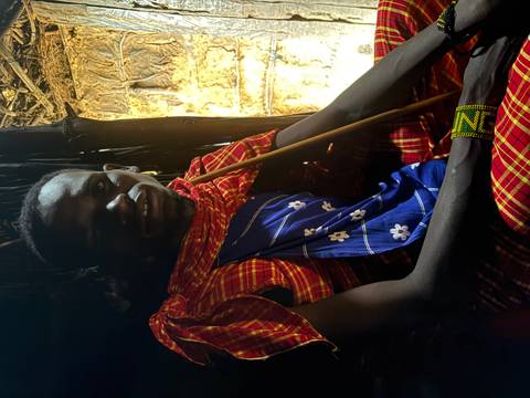 Maasai tribesman in traditional red shuka sitting inside a dimly lit hut