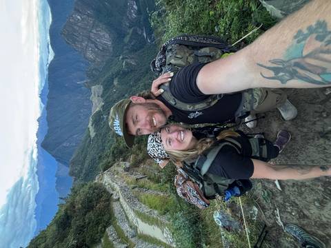 Smiling couple taking a selfie on a mountain trail overlooking Machu Picchu ruins