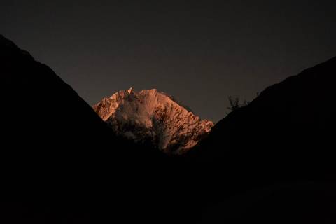 Snowy mountain peak glowing under night sky while surrounding valley remains dark