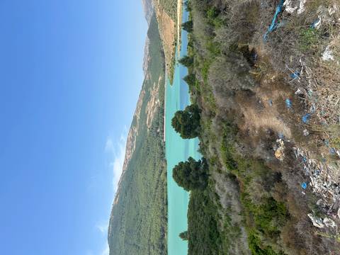 Turquoise reservoir surrounded by rolling green hills with some litter in foreground