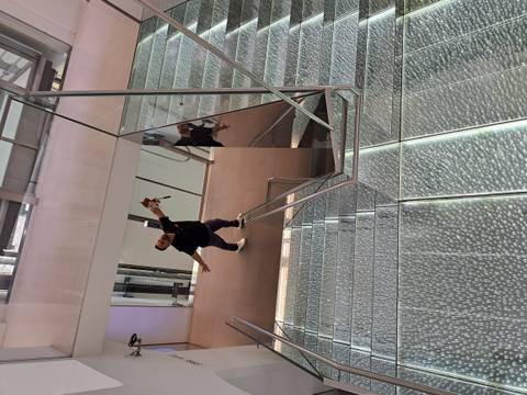 Playful portrait of a traveller stretching arms wide while standing on a futuristic glass staircase inside a modern building.